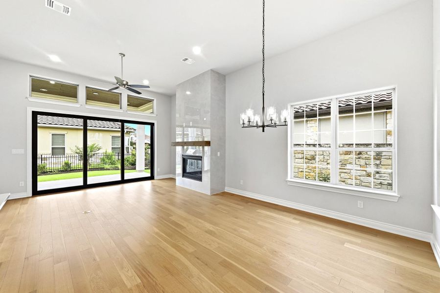 Living area featuring wood-finish flooring, a contemporary chandelier, and a fireplace with a wood mantle and stone surround