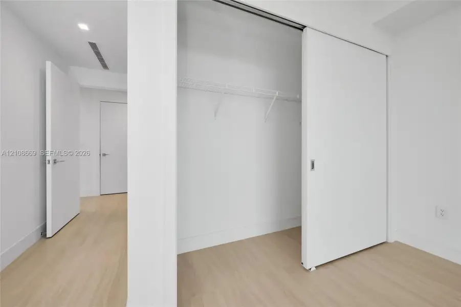 Closet with sliding door, integrated wire shelving, wood-finish flooring, and minimalist interior doors
