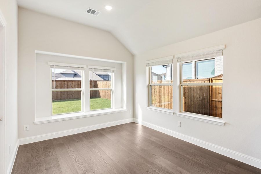 Empty bedroom with vaulted ceiling, hardwood floors, and multiple windows overlooking backyard Empty bedroom with vaulted ceiling, hardwood floors, and multiple windows overlooking backyard