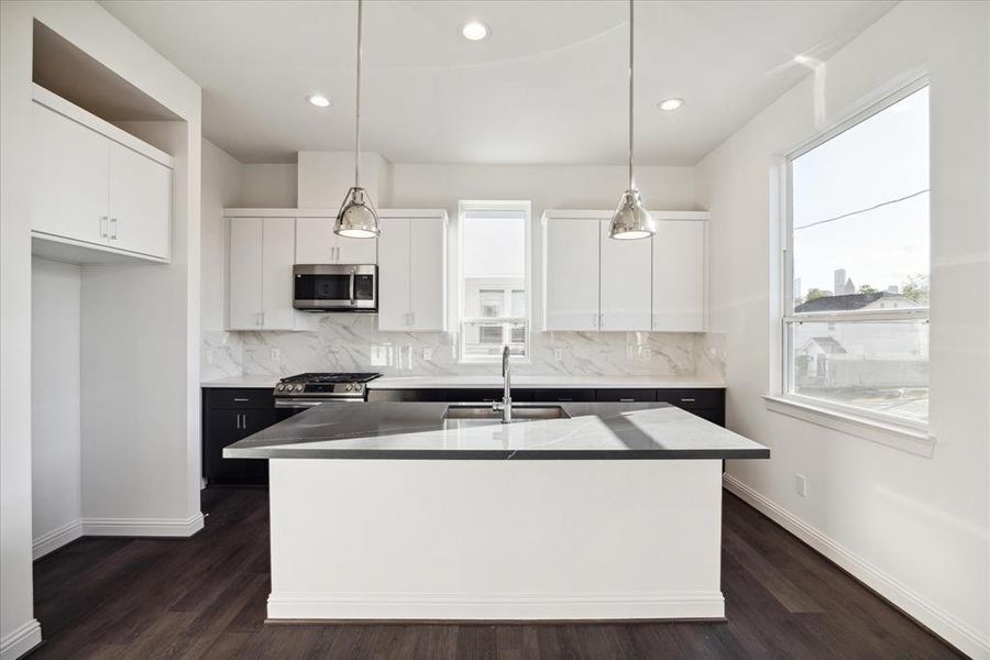 This contemporary kitchen is designed to impress, featuring crisp white cabinetry, a stylish marble-patterned backsplash, and stainless steel appliances. The oversized island with a quartz countertop provides ample workspace and doubles as a gathering spot for family and friends. Pendant lighting adds a touch of elegance, while large windows flood the space with natural light, creating an inviting atmosphere for cooking and entertaining alike.