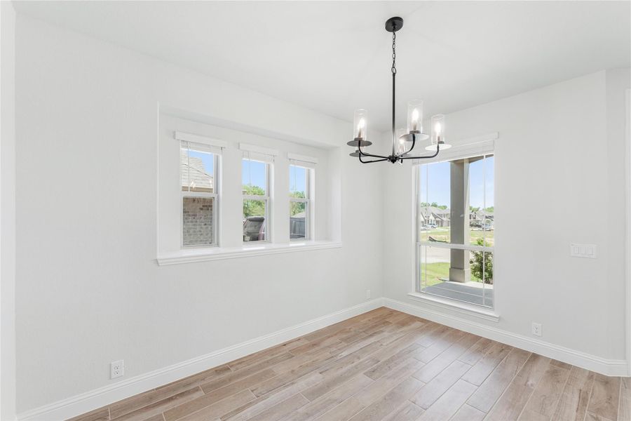 Empty dining room with wood-look floors, white walls, multiple windows, and a black chandelier Empty dining room with wood-look floors, white walls, multiple windows, and a black chandelier