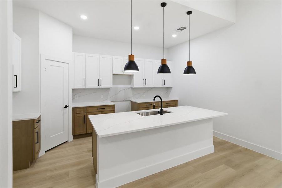 Kitchen with brown cabinetry, hanging light fixtures, white cabinetry, a kitchen island with sink, and light wood finished floors