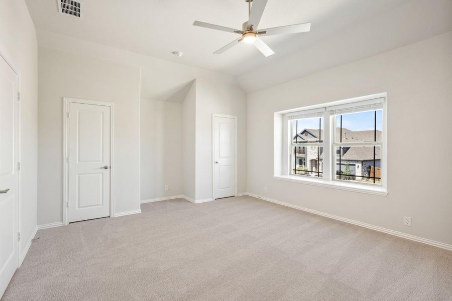 Empty bedroom with vaulted ceiling, ceiling fan, carpet flooring, and large window with neighborhood view Empty bedroom with vaulted ceiling, ceiling fan, carpet flooring, and large window with neighborhood view