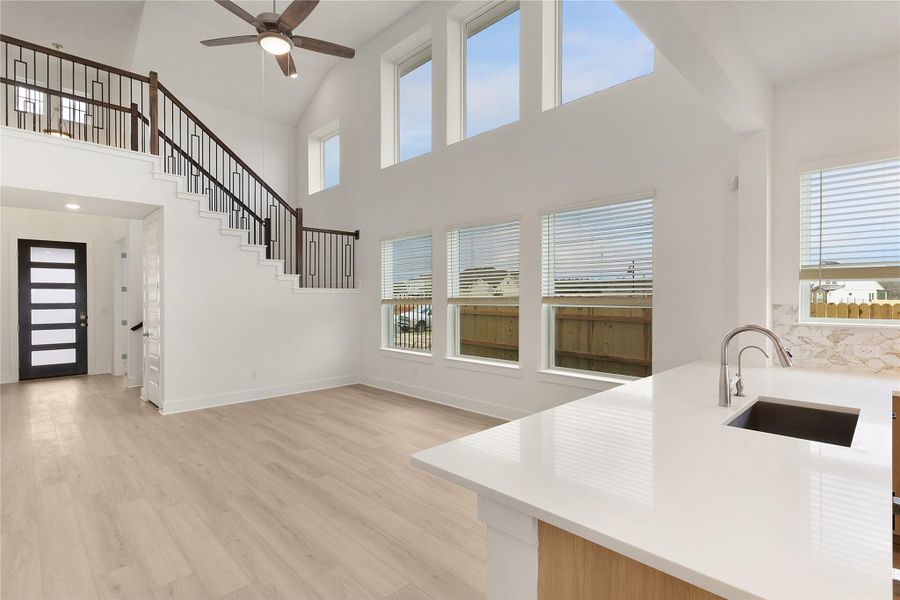 Unfurnished living room featuring light wood-style flooring, a ceiling fan, a towering ceiling, and stairway