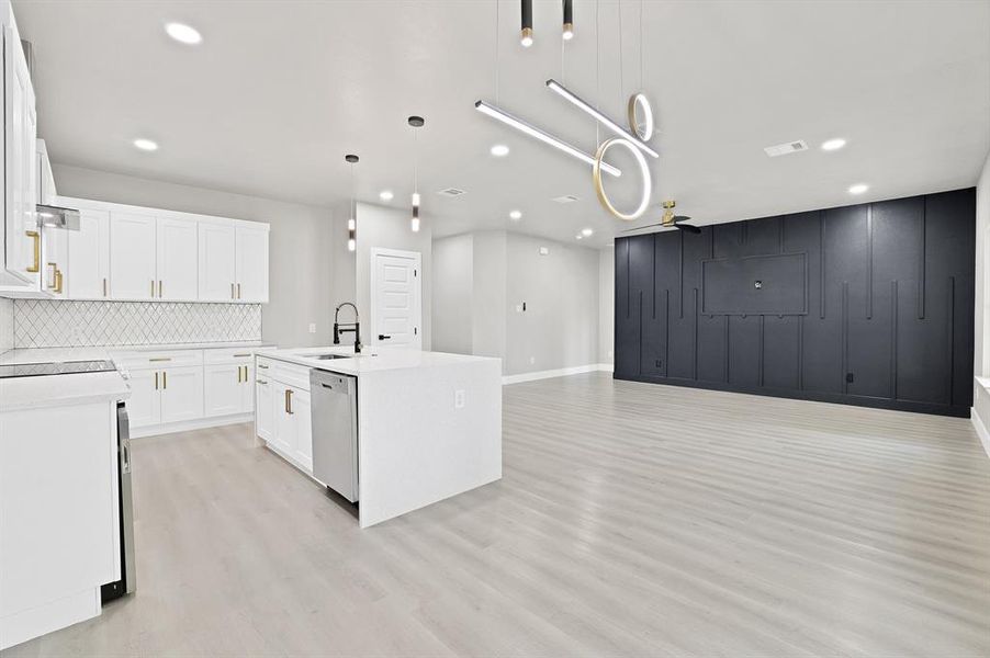 Kitchen with white cabinets, dishwasher, pendant lighting, and a center island with sink