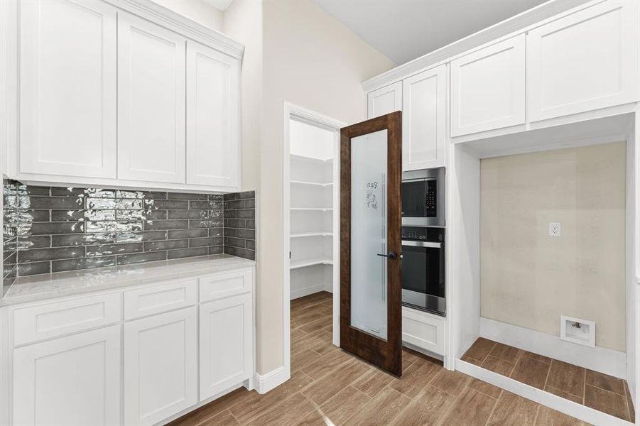 Kitchen with white cabinetry, wood tiled floors, stainless steel appliances, backsplash, and light stone counters