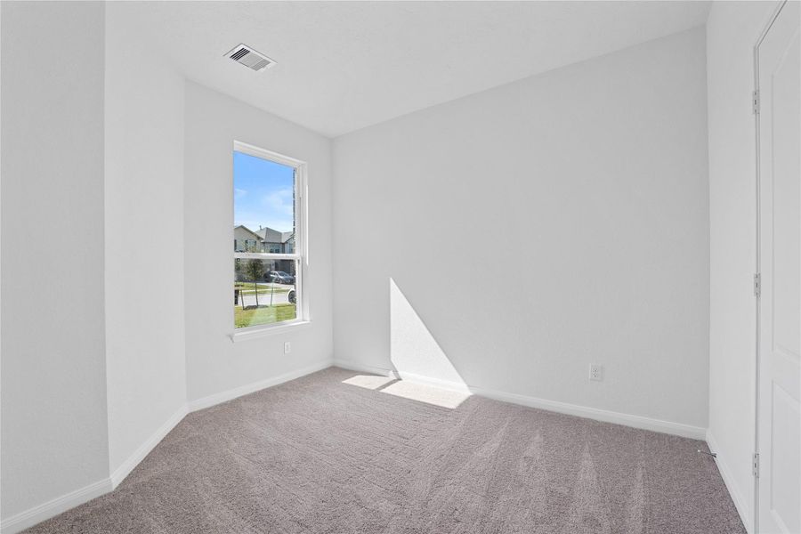 Tucked peacefully in the front of the home, this secondary bedroom offers comfort and style with plush carpeting, neutral paint tones, recessed lighting, a large window, and a generously sized closet