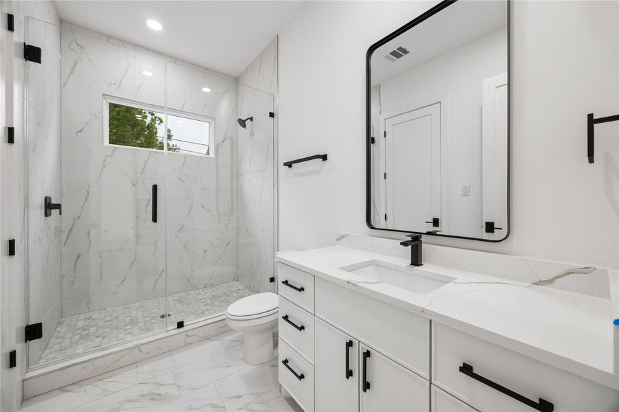 The secondary bathroom features oversized mirrors, contemporary hardware, quartz countertops, and a spacious walk-in shower designed with both functionality and simplicity in mind.