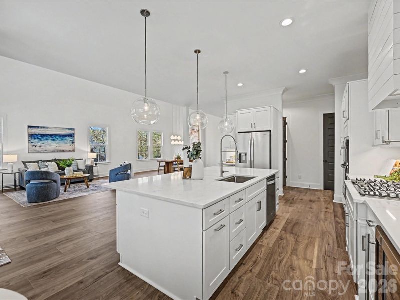 Bright open-concept kitchen with a large quartz island, stainless steel appliances, modern pendant lighting, and seamless flow into the main living area—ideal for entertaining.