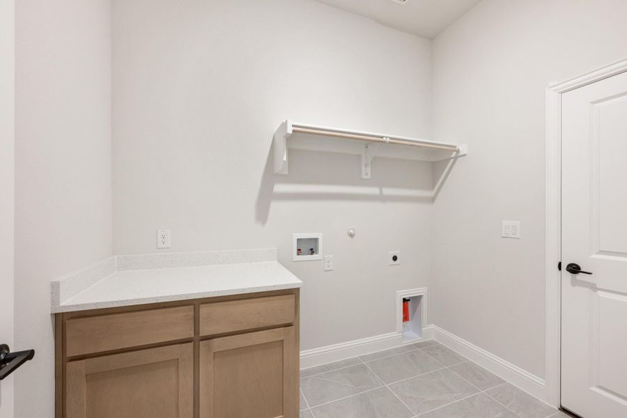 Laundry room with wood cabinets, white countertop, wall shelf, and washer and dryer hookups on tile floor