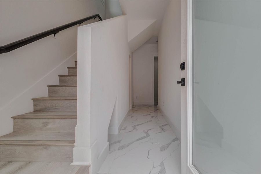 A bright entry area leads into the home with a modern staircase, white walls, and light flooring. The clean palette creates an immediate sense of openness and sets the tone for the contemporary interior throughout.