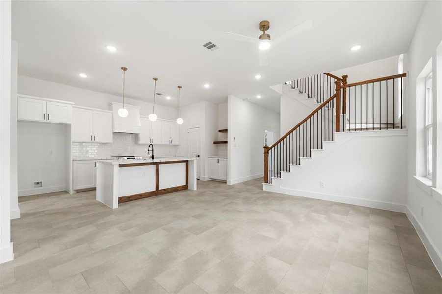 This stunning open-concept living space is bathed in natural light from large windows, complementing the neutral-toned flooring. A statement staircase with wood handrails and sleek black metal balusters adds a sophisticated focal point, leading to the second level.