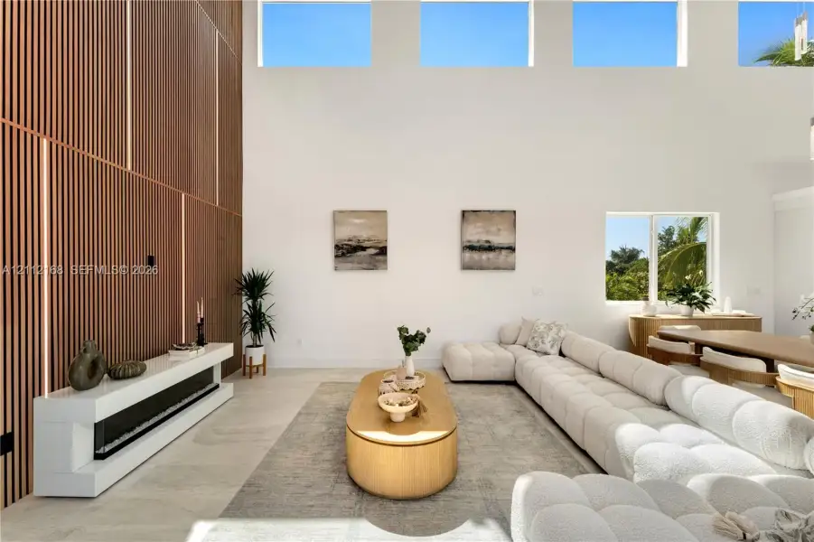 Double-height ceilings with transom windows, full-height vertical wood-slat feature wall, integrated linear fireplace with white floating hearth, and large-format tile flooring Double-height ceilings with transom windows, full-height vertical wood-slat feature wall, integrated linear fireplace with white floating hearth, and large-format tile flooring