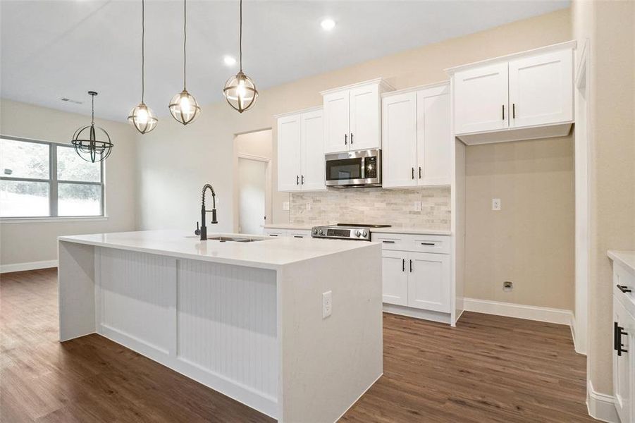 Kitchen featuring an island with sink, dark wood-type flooring, stainless steel appliances, sink, and decorative backsplash