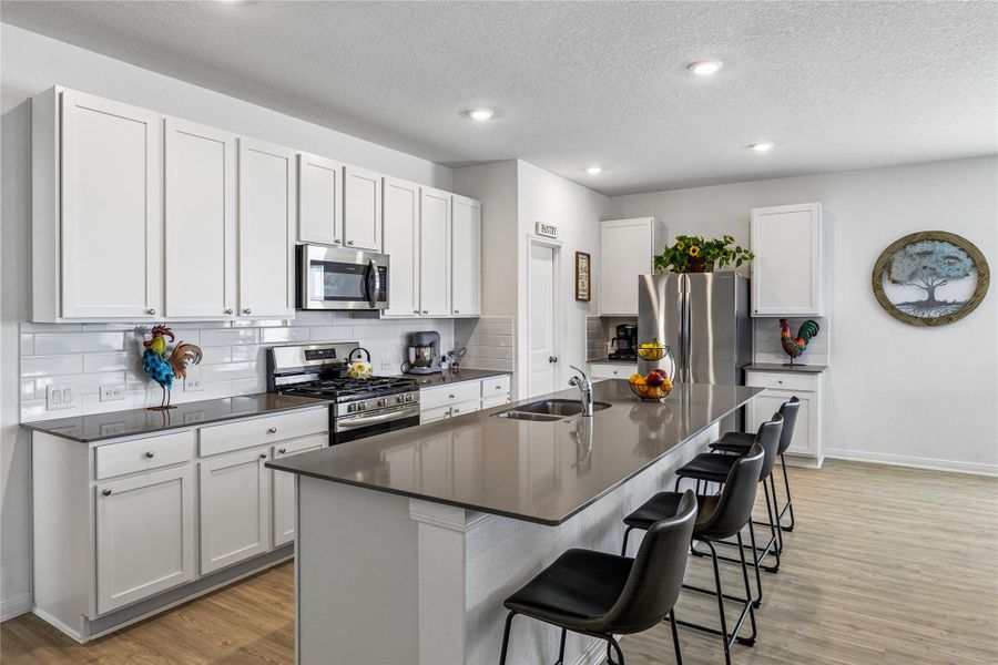 Kitchen featuring white shaker cabinetry, stainless steel appliances, dark countertops, a subway tile backsplash, and an extended island with seating Kitchen featuring white shaker cabinetry, stainless steel appliances, dark countertops, a subway tile backsplash, and an extended island with seating