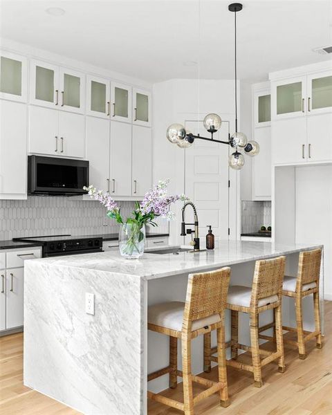 Kitchen with decorative light fixtures, light hardwood / wood-style floors, electric range, and a center island with sink