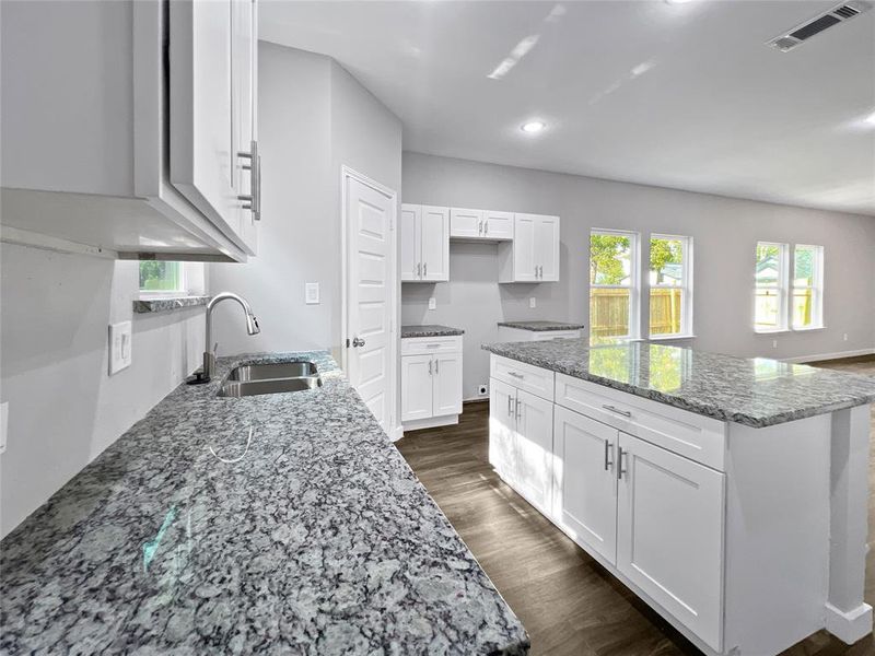 Kitchen with sink, light stone counters, dark hardwood / wood-style flooring, and white cabinetry