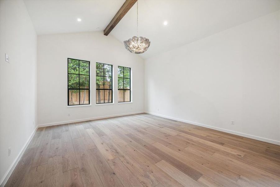 The spacious first floor primary bedroom features vaulted ceilings with exposed beams and large windows that overlook the private backyard, creating a serene retreat.