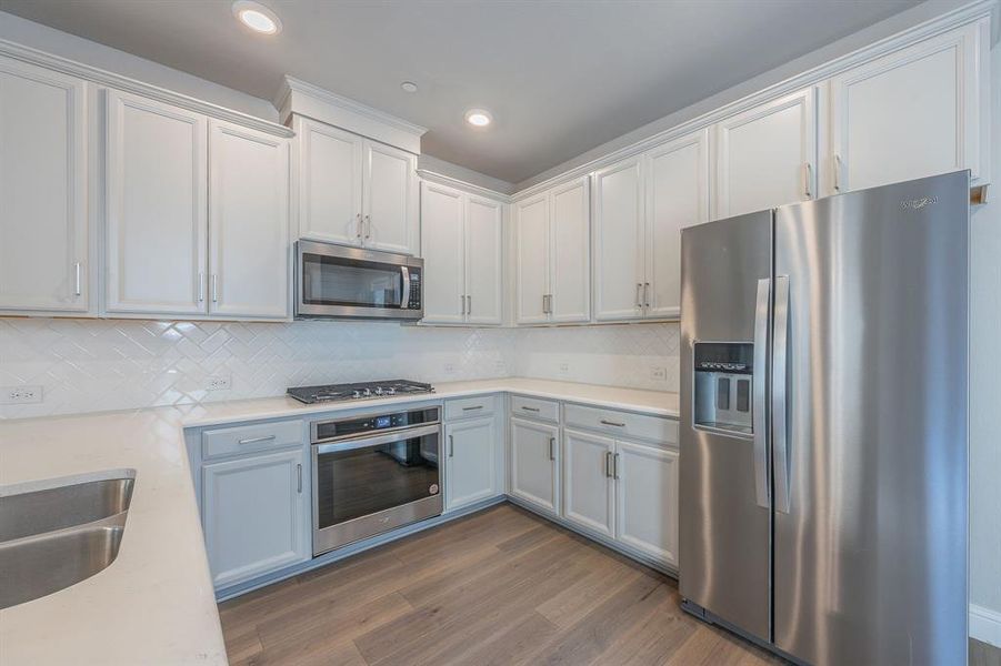 Kitchen with quartz countertops, decorative backsplash, gas range vented to the exterior of the home, white cabinetry with door handles and a new stainless steel refrigerator that can convey to the new buyer - View