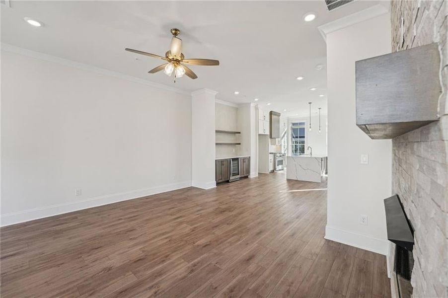 Unfurnished living room with recessed lighting, dark wood-style flooring, ornamental molding, a ceiling fan, and beverage cooler Unfurnished living room with recessed lighting, dark wood-style flooring, ornamental molding, a ceiling fan, and beverage cooler