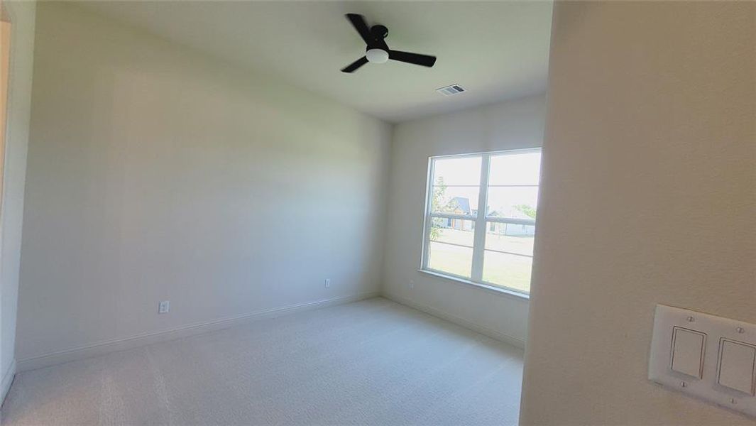 Neutral-toned room featuring a large window, light-colored carpeting, a ceiling fan with black blades, and contemporary white wall switches