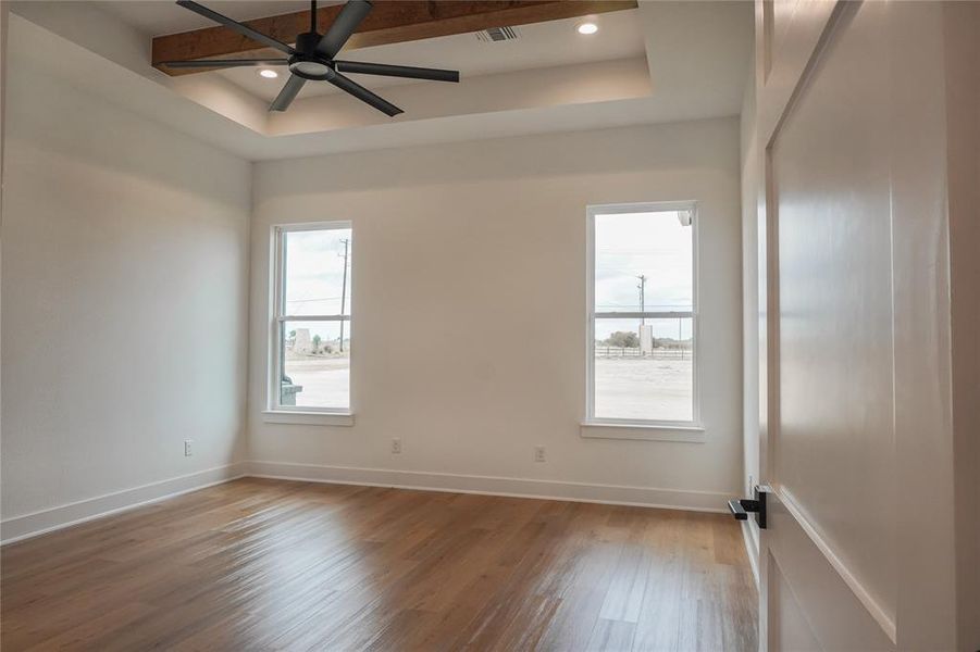 Unfurnished room featuring a raised ceiling, hardwood / wood-style flooring, ceiling fan, and beam ceiling