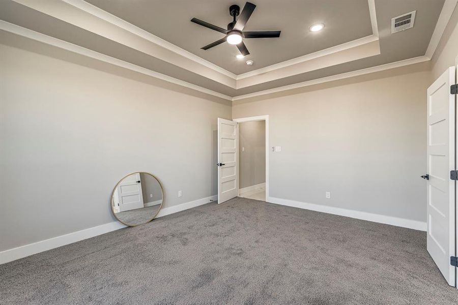 Unfurnished bedroom with a raised ceiling, visible vents, and ornamental molding