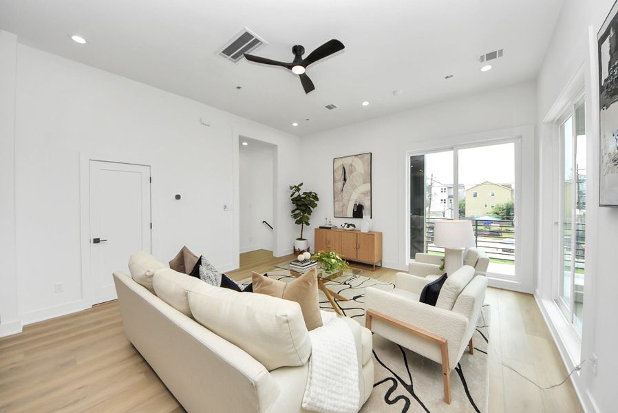 Bright living room featuring modern seating, oversized windows, and access to the private balcony.