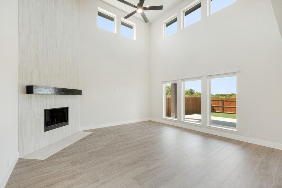Open living room with two-story ceiling, tile fireplace, ceiling fan, and wood-look floors