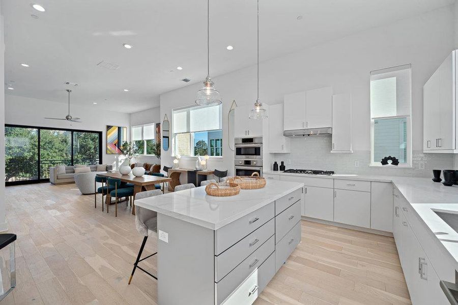 Kitchen with a kitchen breakfast bar, light wood-type flooring, white cabinetry, pendant lighting, and a kitchen island