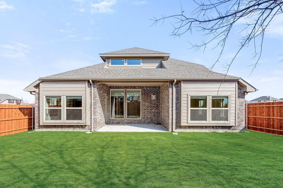 Rear exterior of brick home with hip roof, covered patio, and fenced backyard with green lawn Rear exterior of brick home with hip roof, covered patio, and fenced backyard with green lawn