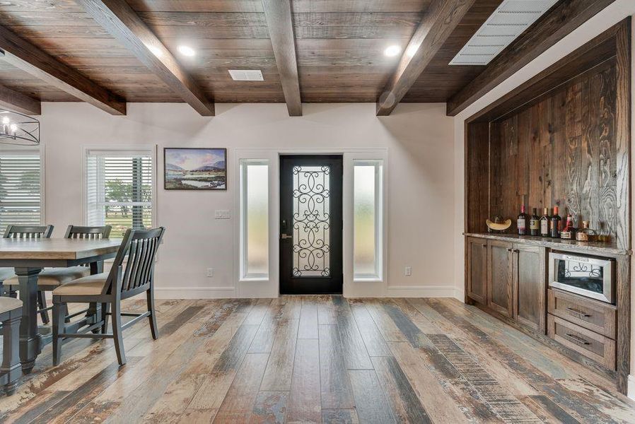 Entryway featuring a decorative wrought iron door, wood-finish flooring, exposed wood beam ceiling, and a built-in beverage bar with wood paneling and stone countertop Entryway featuring a decorative wrought iron door, wood-finish flooring, exposed wood beam ceiling, and a built-in beverage bar with wood paneling and stone countertop