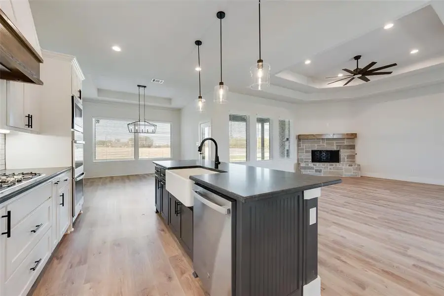 Open-concept kitchen and living area featuring wood-finish flooring, a kitchen island with a farmhouse sink, stainless steel appliances, and pendant lighting