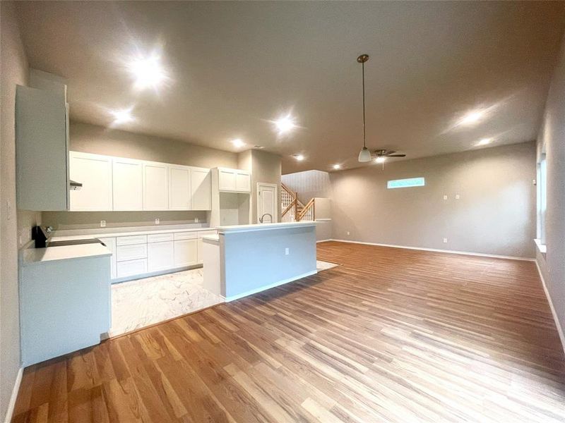 Kitchen featuring light wood finished floors, a kitchen island with sink, white cabinets, baseboards, and a ceiling fan