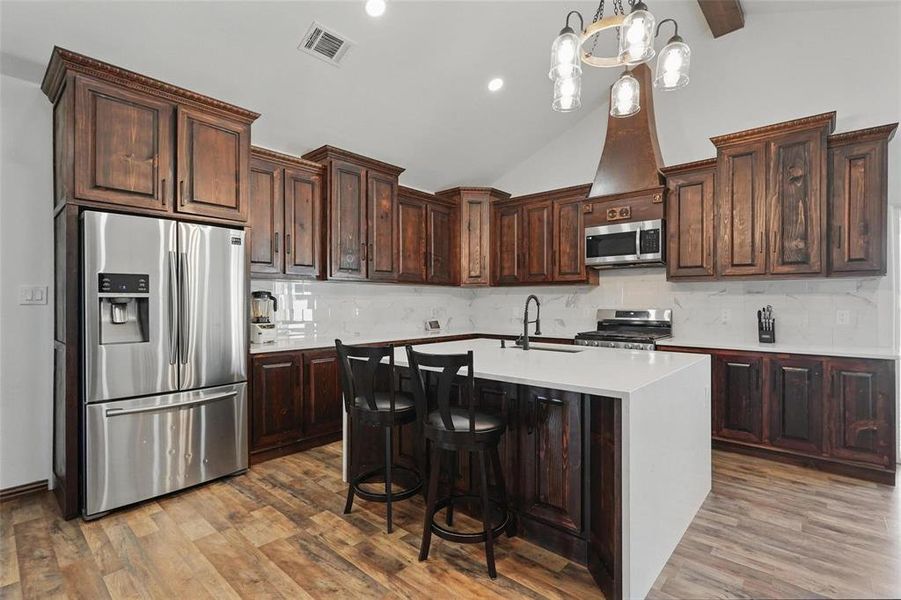 Kitchen with stainless steel appliances, an island with sink, pendant lighting, a breakfast bar area, and dark brown cabinets Kitchen with stainless steel appliances, an island with sink, pendant lighting, a breakfast bar area, and dark brown cabinets