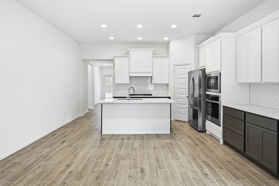 Sleek modern kitchen with white cabinetry, stainless steel appliances, and a spacious island, complemented by elegant wood-look flooring and recessed lighting.