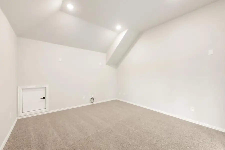Empty bonus room with vaulted ceiling, beige carpet, and small access door on white walls Empty bonus room with vaulted ceiling, beige carpet, and small access door on white walls