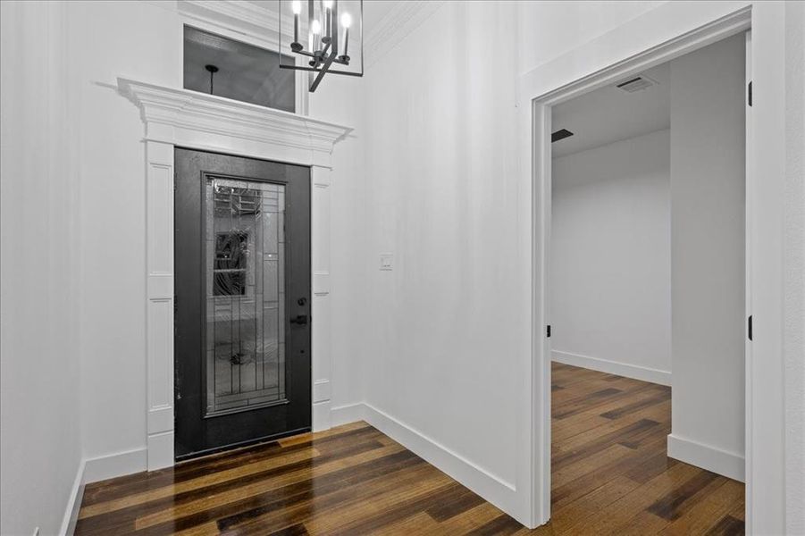 Foyer entrance with wood-style floors, a chandelier, and crown molding