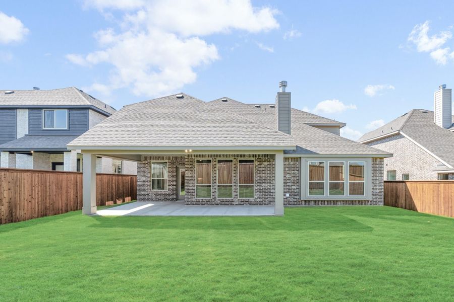 Brick home rear exterior with covered patio, large green lawn, and wood privacy fence