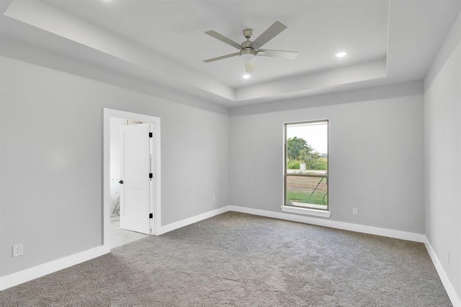 Empty room with a raised ceiling, light colored carpet, recessed lighting, and a ceiling fan