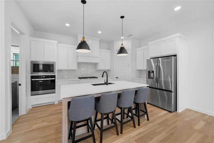 Contemporary kitchen featuring a large central island, white cabinetry, stainless steel appliances, and wood-finish flooring