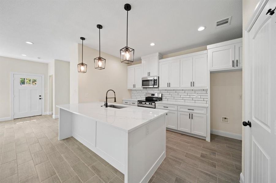 Kitchen featuring backsplash, sink, stainless steel appliances, and white cabinetry