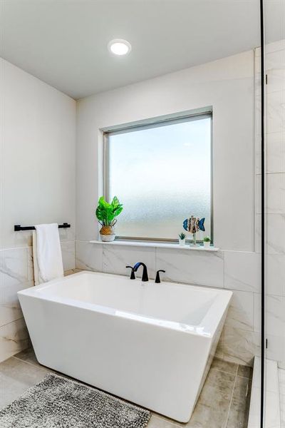 Bathroom with tile patterned flooring, a washtub, tile walls, and a wealth of natural light