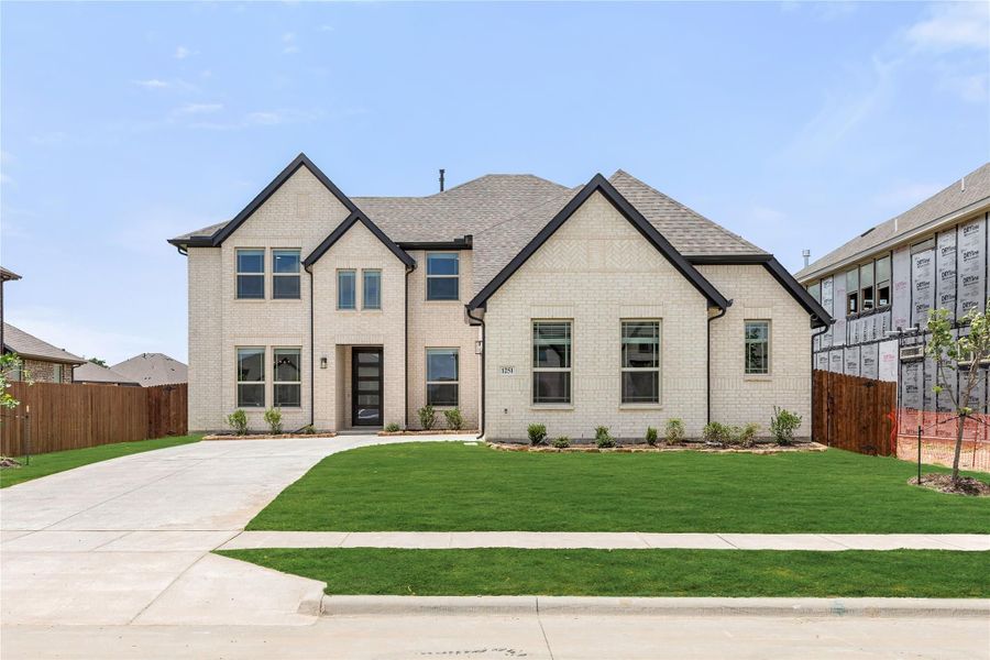 Two-story brick home with dark trim, wide driveway, and manicured front lawn