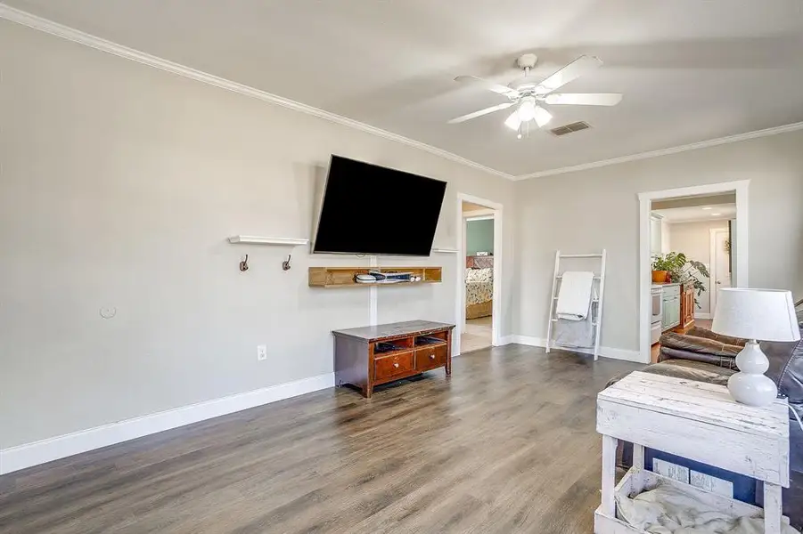 Living area featuring dark wood-style flooring, ceiling fan, and crown molding