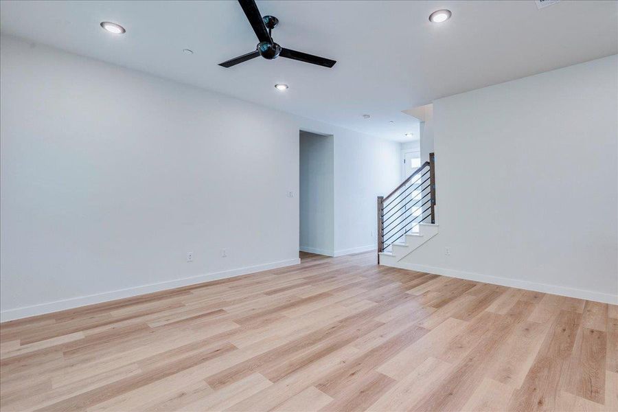 A spacious, open-concept living area with light-toned hardwood flooring leads to a modern staircase.