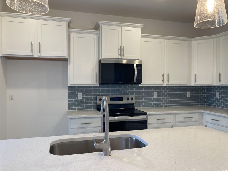 Kitchen featuring hanging light fixtures, stainless steel appliances, white cabinetry, tasteful backsplash, and light stone countertops