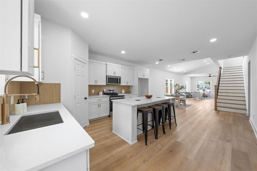 Kitchen featuring appliances with stainless steel finishes, a breakfast bar area, white cabinets, a center island, and light countertops Kitchen featuring appliances with stainless steel finishes, a breakfast bar area, white cabinets, a center island, and light countertops