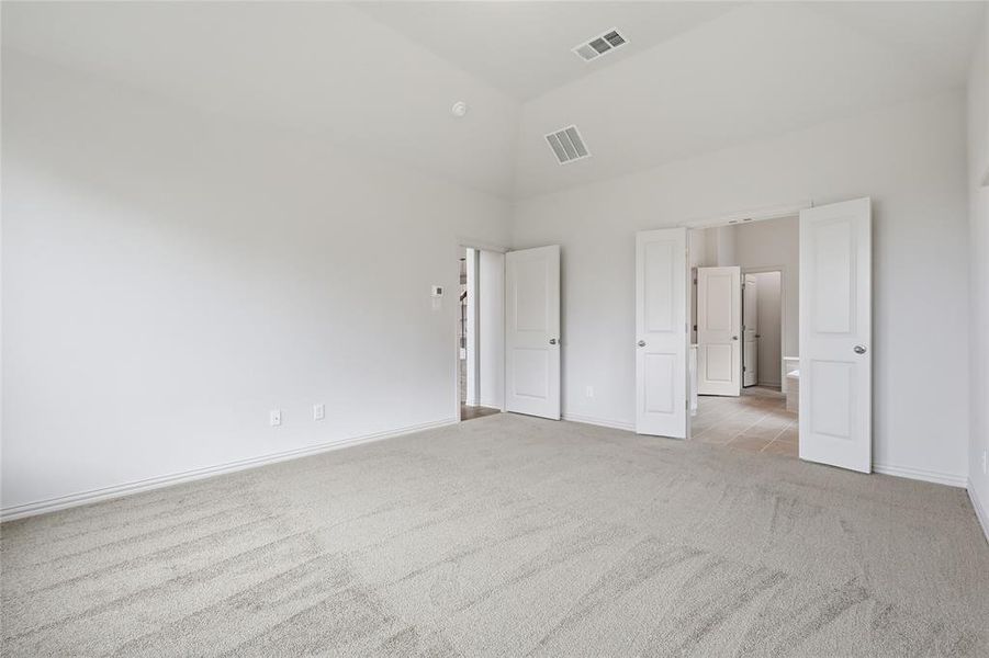 Spacious carpeted room featuring a vaulted ceiling and multiple white panel doors