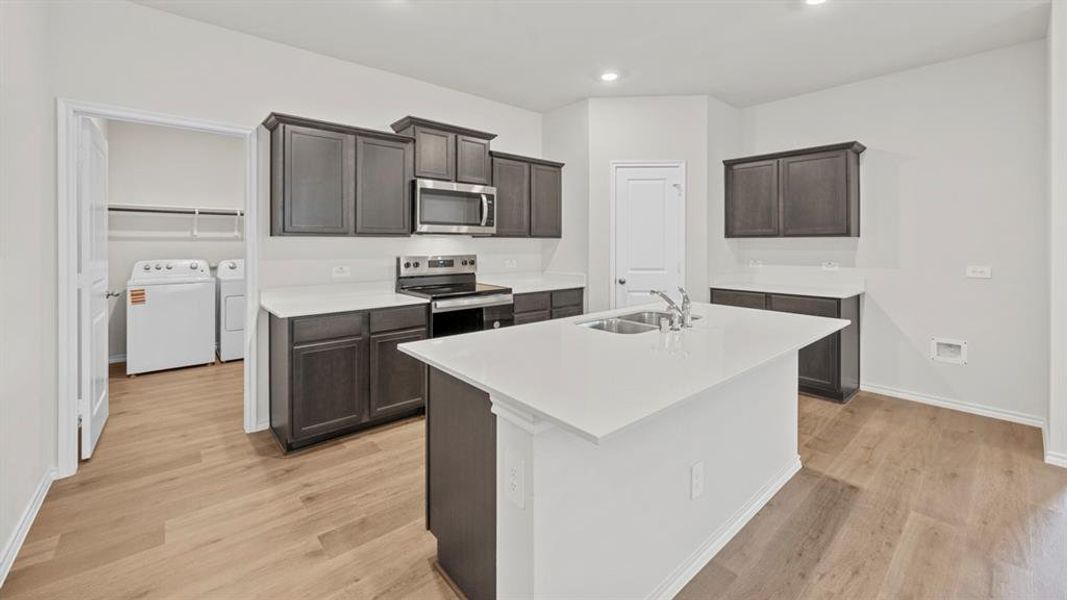 Kitchen with stainless steel appliances, a kitchen island with sink, independent washer and dryer, light wood finished floors, and recessed lighting